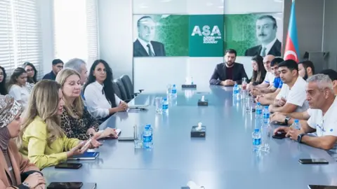 Güləşçilər məşq edir, kənarda fizioterapist müşahidə edir