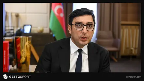 Fərid Qayıbov mikrofona danışır, arxa planda ultramarafon iştirakçıları