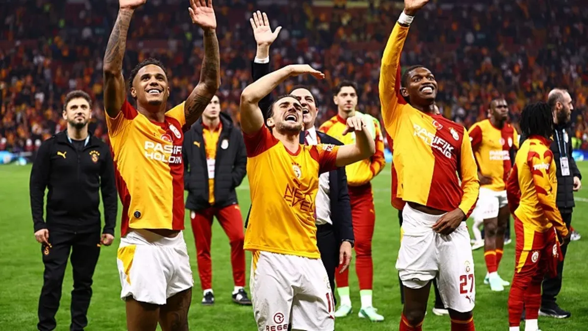 Galatasaray oyuncuları derbi sonrası seviniyor, taraftarlar tribünde büyük bayrak sallıyor