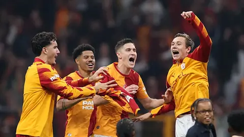 Galatasaray oyuncuları orta sahada kutlama yaparken, tribünde taraftarlar ve Dursun Özbek