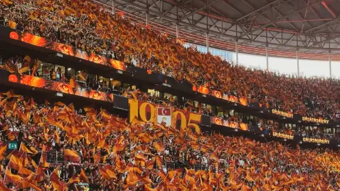 Galatasaray ve Fenerbahçe logoları ile dolu bir stadyum tribünü görüntüsü