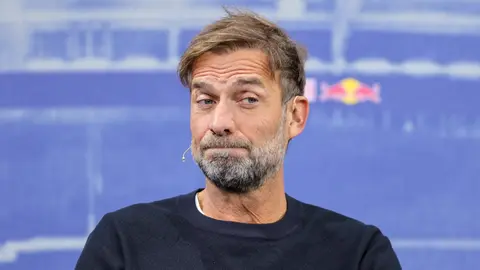 Yurgen Klopp danışarkən mikrofona baxır, fonunda futbol stadionu