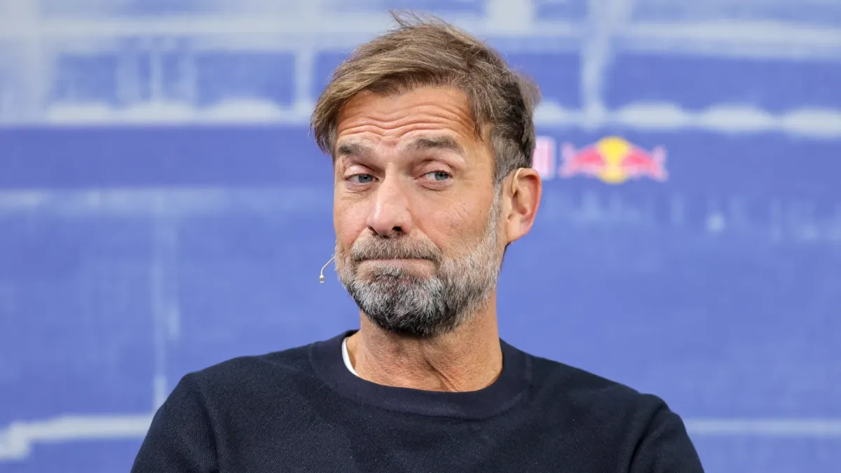 Yurgen Klopp danışarkən mikrofona baxır, fonunda futbol stadionu