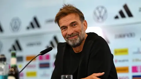 Yurgen Klopp mikrofon qarşısında danışır, arxa planda futbol stadionu