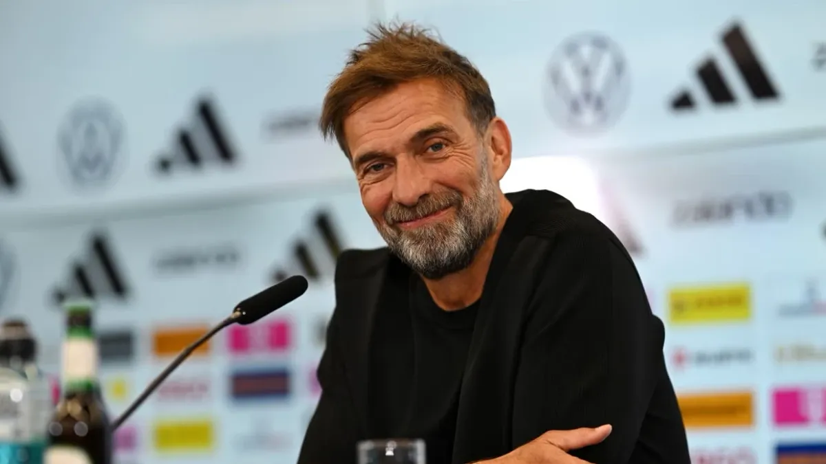 Yurgen Klopp mikrofon qarşısında danışır, arxa planda futbol stadionu