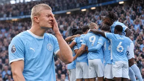 Manchester City forması giyen bir grup futbolcu ve kulüp binası