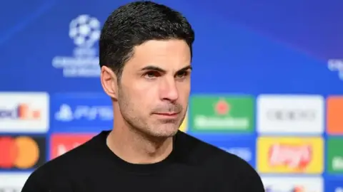 Mikel Arteta mətbuat konfransında danışır, Arsenal loqosu fonunda