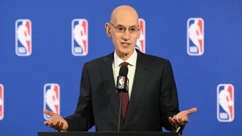 NBA logosu ve salon içerisinde basketbol maçı oynanan bir an