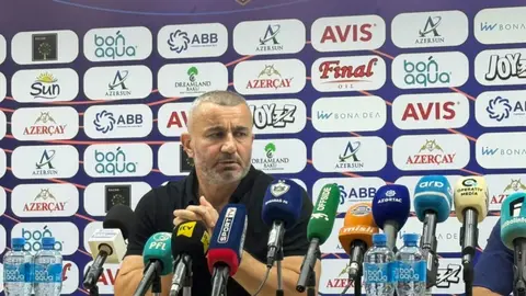Qurban Qurbanov mətbuat konfransında, arxa planda futbol stadionu