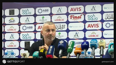 Qurban Qurbanov mətbuat konfransında, arxa planda futbol stadionu