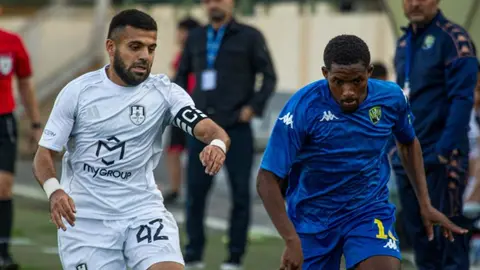 Rəhim Həsənov danışır, arxa planda futbol meydançası