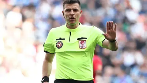 Ümit Öztürk maç yönetirken saha kenarında düdük ve hakem formasıyla