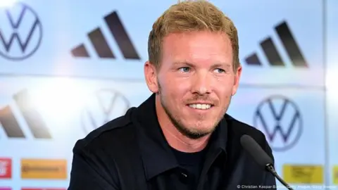 Yulian Naqelsmann ağ kostyumda stadion kənarında